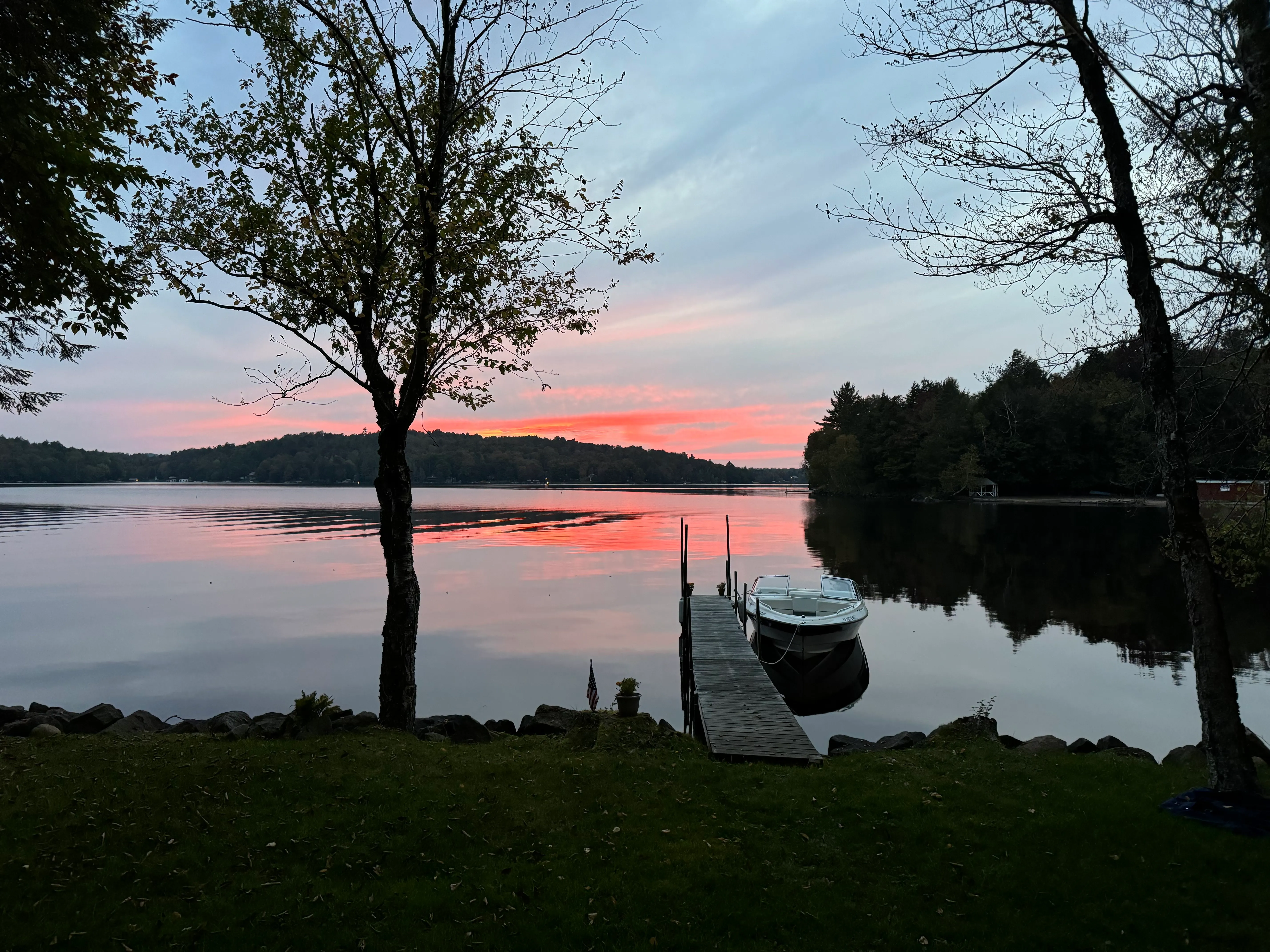 Sunset over Cranberry Lake from Tilly's, with a small boat tied to a wooden dock and pink clouds reflected in still water.